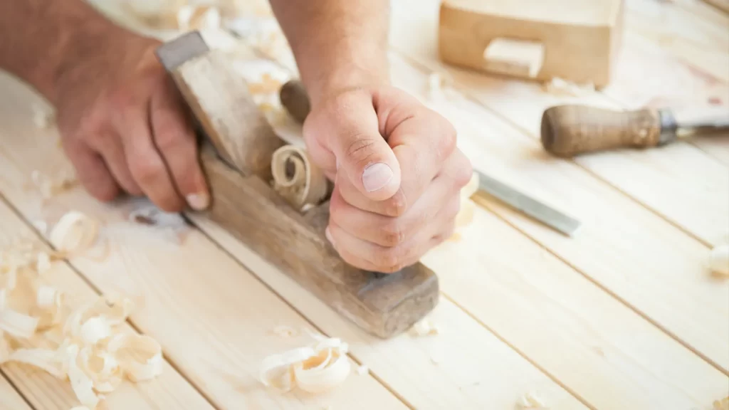 A hand plane smoothing the Best Wood for Carving, revealing natural grain patterns and fine wood shavings.